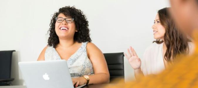 Image of a person sitting behind a laptop with others around. Image courtesy of Christina @ wocintechchat via Unsplash