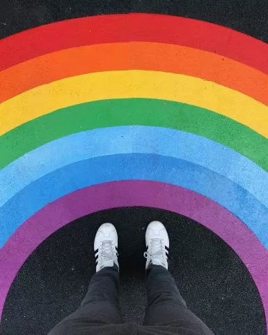 Image of someone standing in front of a rainbow. 