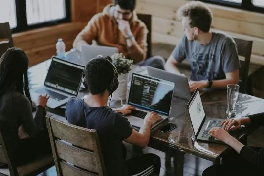 Image of a workplace; people sitting around a table with laptops; Photo by Annie Spratt on Unsplash