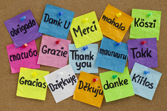 Cork board full of multi-colored post-it notes saying "thank you" in different languages.